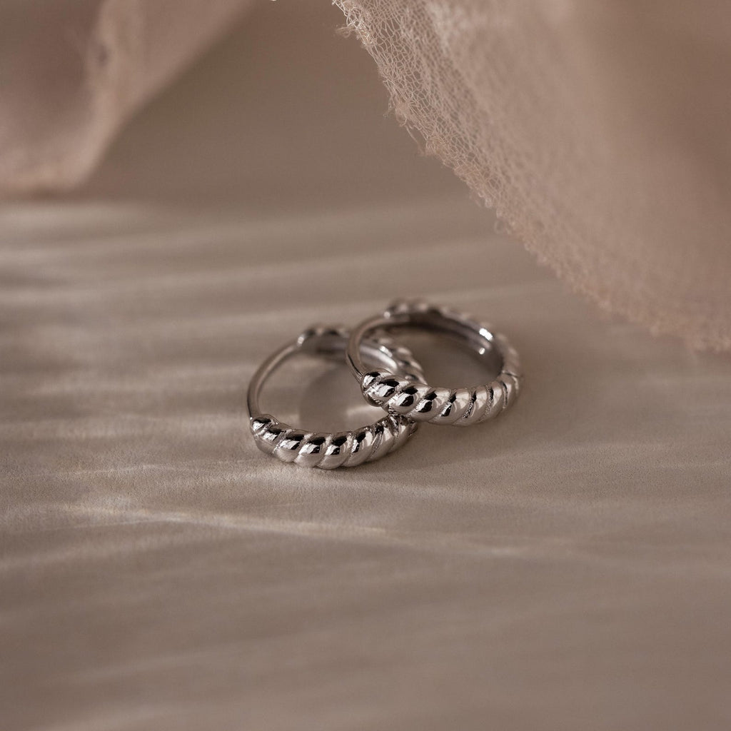 Pair of silver twisted hoop earrings on a textured beige surface