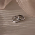 Pair of silver twisted hoop earrings on a textured beige surface