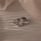 Pair of silver twisted hoop earrings on a textured beige surface