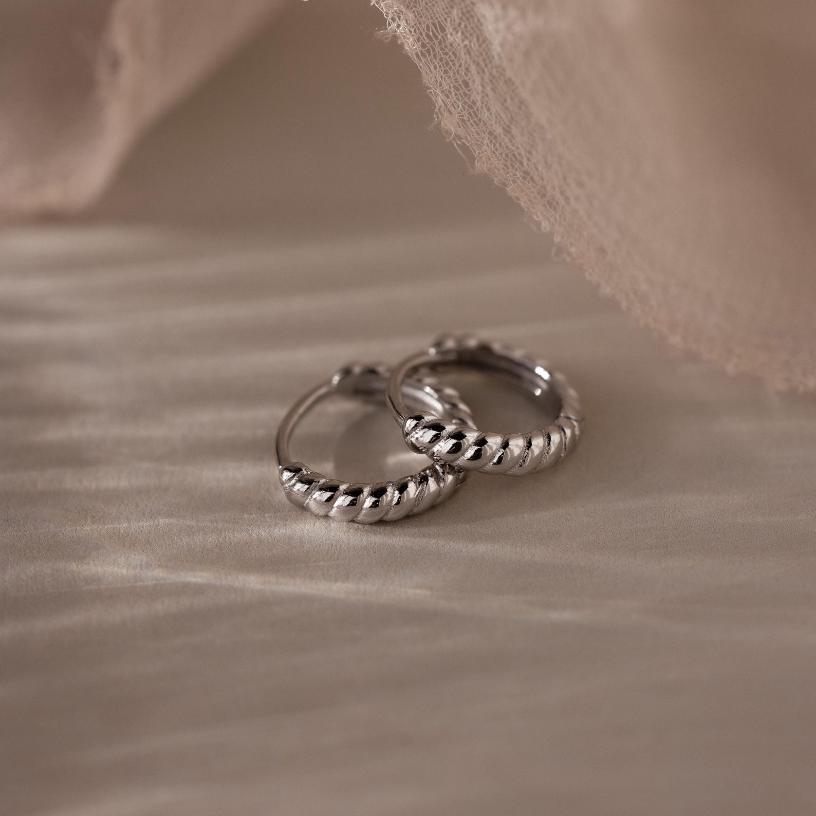 Pair of silver twisted hoop earrings on a textured beige surface
