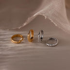 Four gold and silver hoop earrings on a textured beige surface