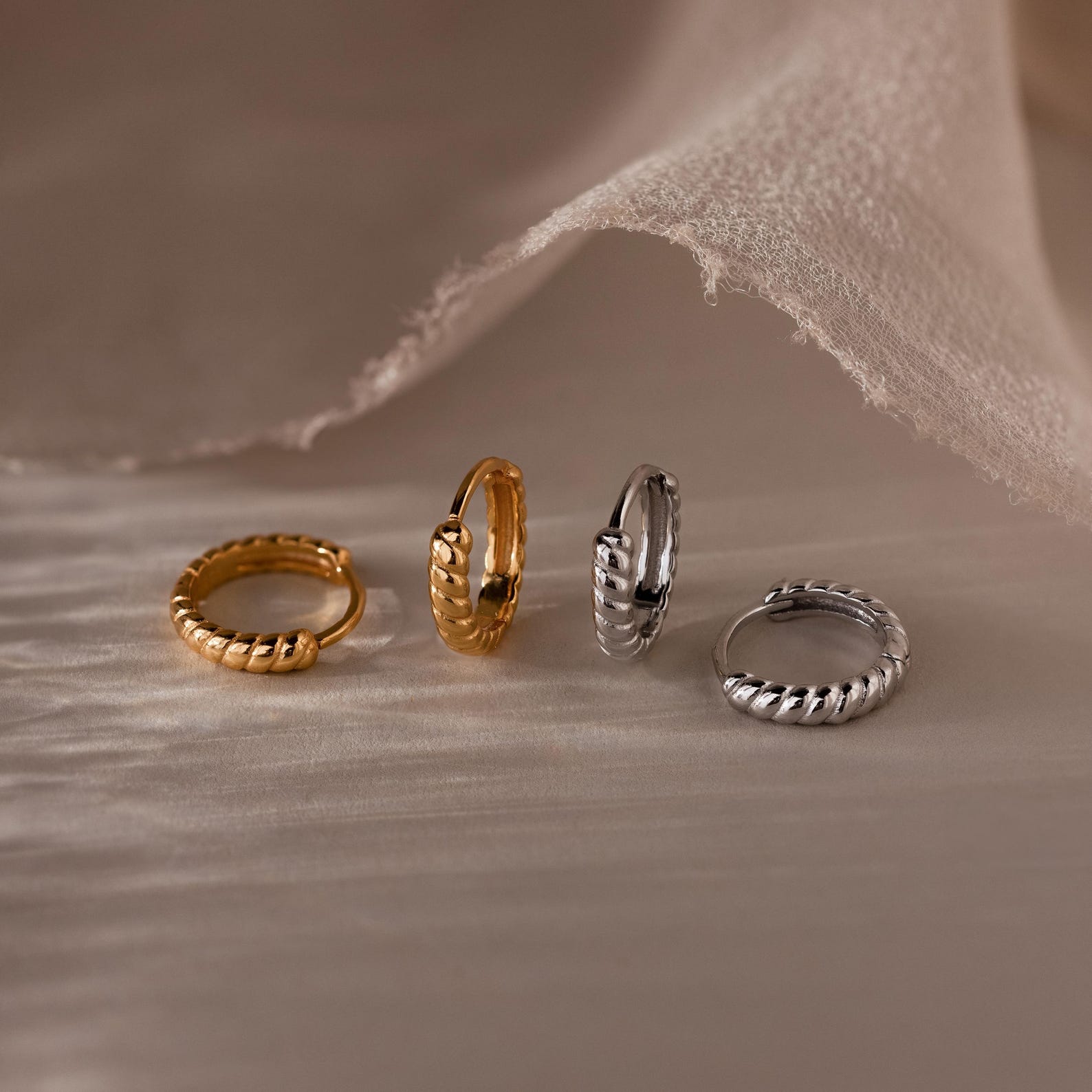 Four gold and silver hoop earrings on a textured beige surface