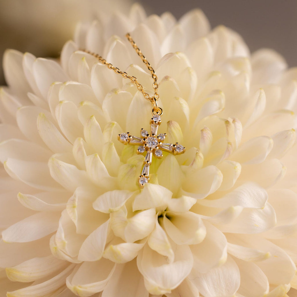 The Vintage Diamond Cross Necklace in 18K Gold features small diamonds set in a gold cross, displayed on a large, pale cream flower—an elegant and timeless vintage piece.