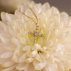 The Vintage Diamond Cross Necklace in 18K Gold features small diamonds set in a gold cross, displayed on a large, pale cream flower—an elegant and timeless vintage piece.