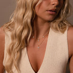 A woman with long blonde hair wears layered gold necklaces, including the Vintage Diamond Cross Necklace in 18K Gold, along with a cream sleeveless knit top.