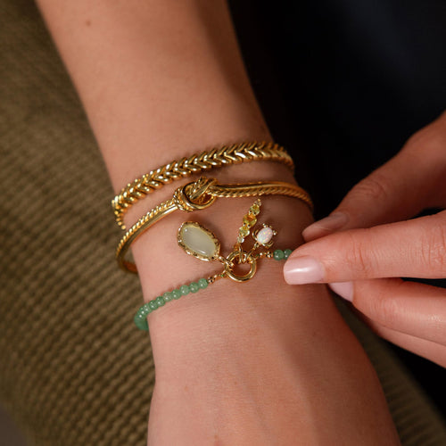 Aura Seafoam Charm, a soft seafoam stone in an organic gold setting, on a wrist with other gold bracelets.