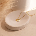 The Add-On Listing features a gold initial necklace with two small letter pendants displayed on a white ceramic dish, set against a neutral background. Ideal for personalizing your order or as an extra to your custom selection.