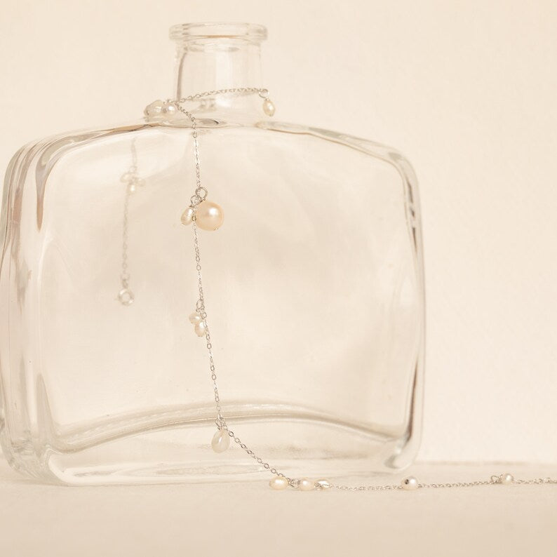The Baroque Pearl Station Necklace in Sterling Silver is elegantly displayed on a clear glass bottle against a neutral background, making it the perfect wedding jewelry.