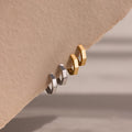 Two pairs of gold and silver geometric hoop earrings on a beige background