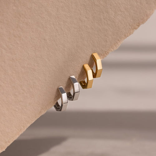 Two pairs of gold and silver geometric hoop earrings on a beige background