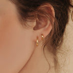 Close-up of a woman's ear with two Editor Huggies in gold and wavy brown hair, highlighting a minimal aesthetic.