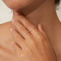 A hand with nude nails, adorned with the Thin Stacking Rings Set in Sterling Silver, gently touches a woman's neck.