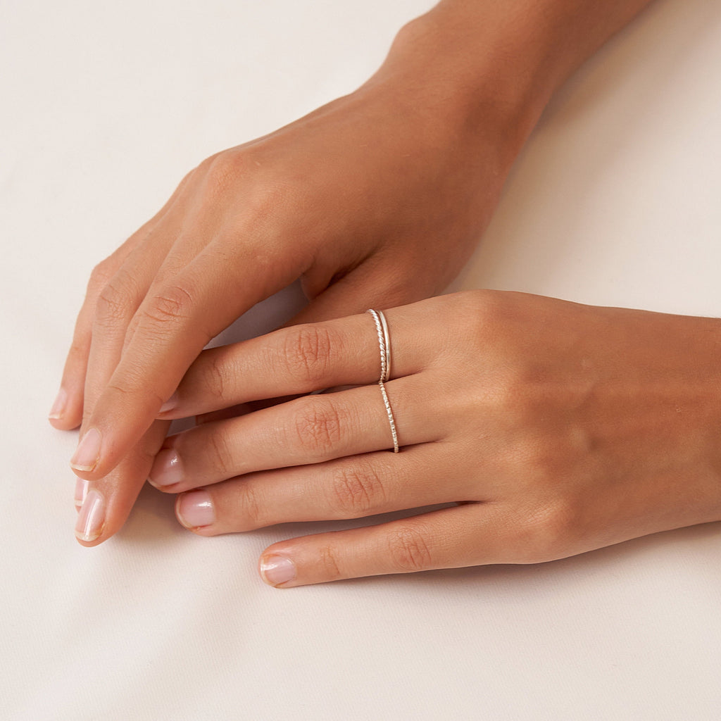 Two hands on a white surface, one adorned with the Thin Stacking Rings Set in Sterling Silver—an elegant and stylish Christmas gift choice.