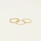 The Thin Stacking Rings Set features three delicate gold rings with unique textures, creating a stunning stack. Perfect as a Christmas gift, they're beautifully displayed on a simple light background.