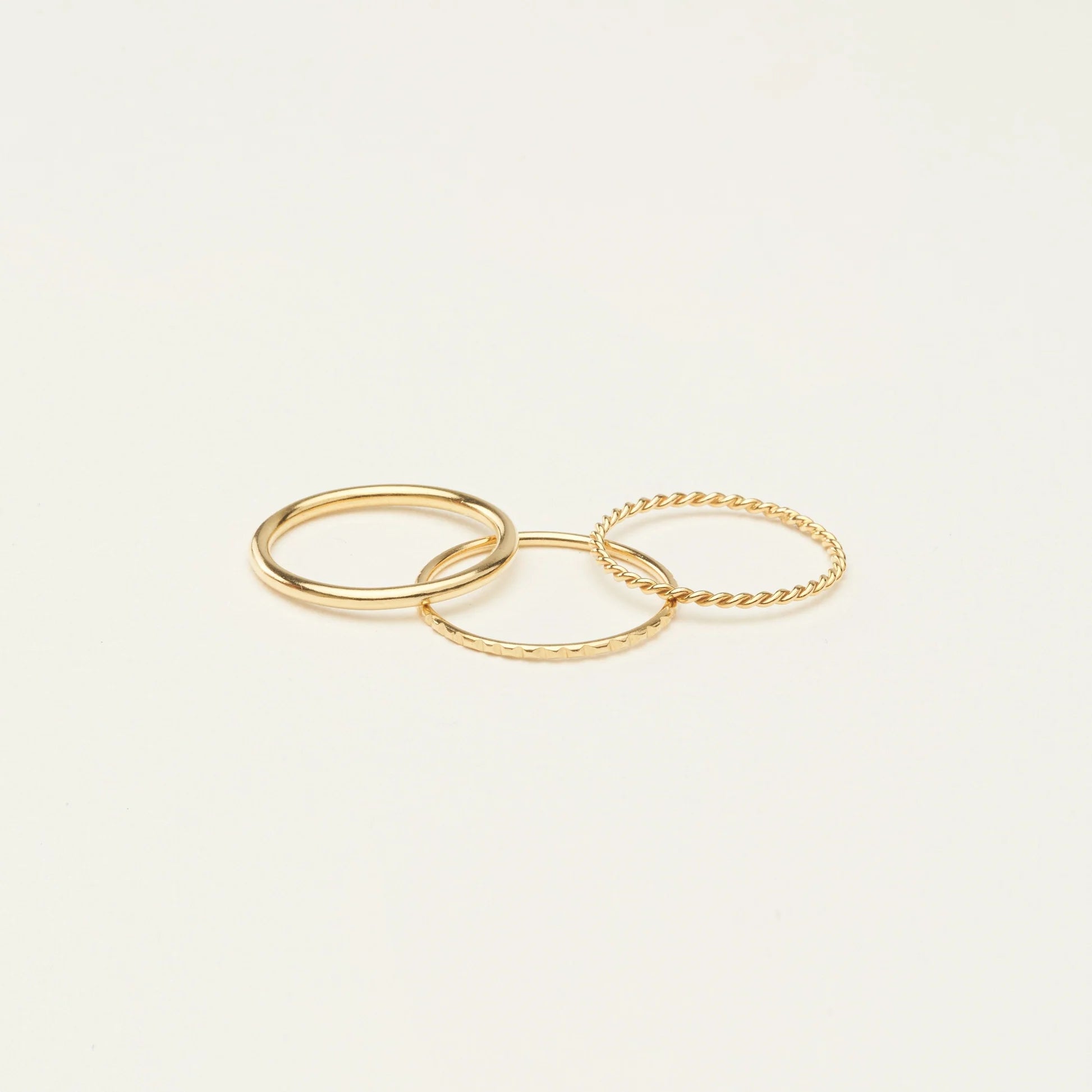 The Thin Stacking Rings Set features three delicate gold rings with unique textures, creating a stunning stack. Perfect as a Christmas gift, they're beautifully displayed on a simple light background.