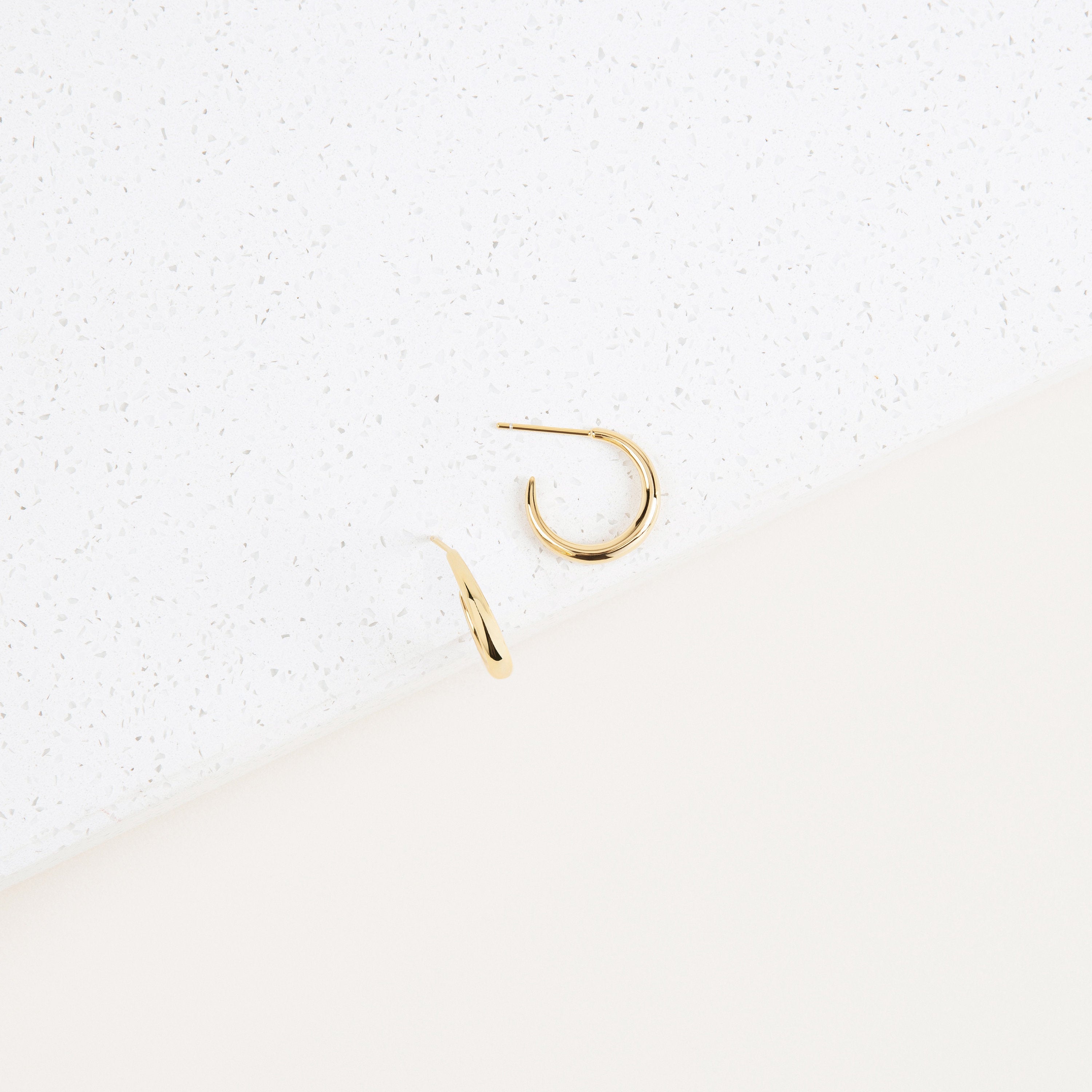 Gold stud hoop earrings on a textured white background