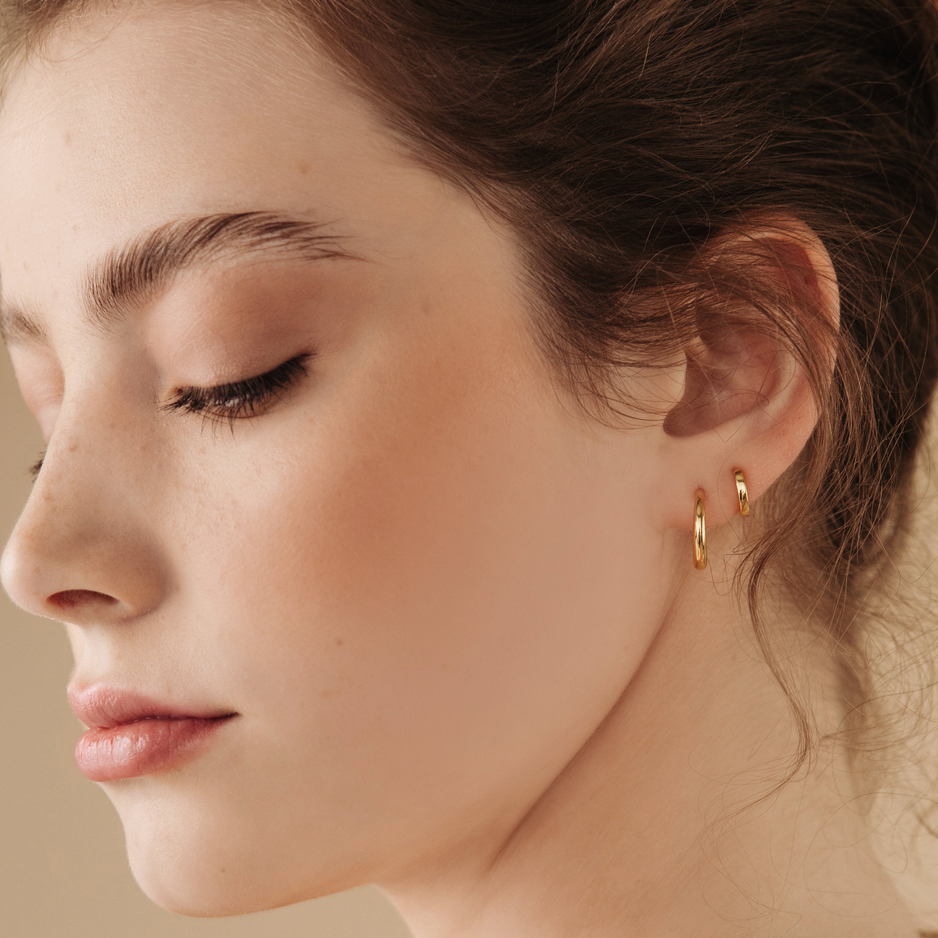 Close-up of a woman wearing gold hoop earrings with a neutral background