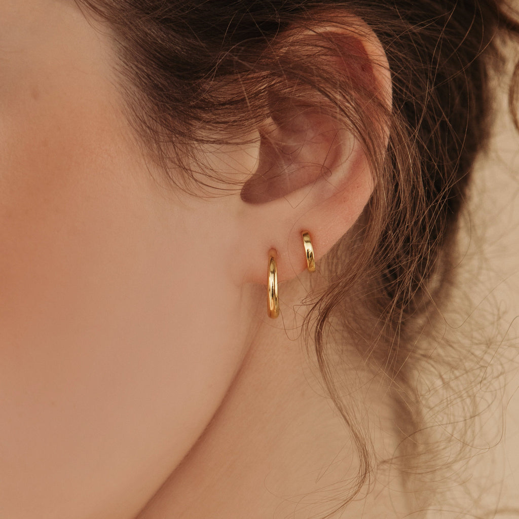 Close-up of a model wearing two gold hoop earrings with a blurred background