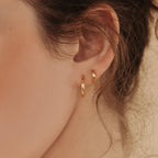Close-up of a model wearing two gold hoop earrings with a blurred background