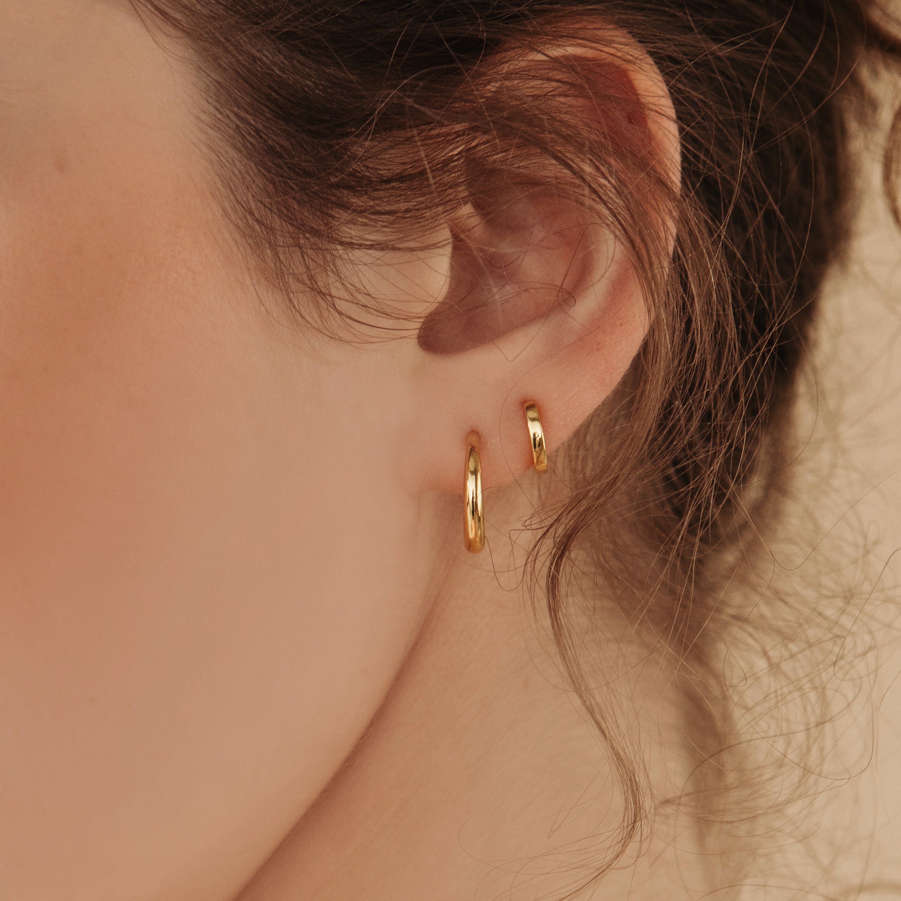 Close-up of a model wearing two gold hoop earrings with a blurred background