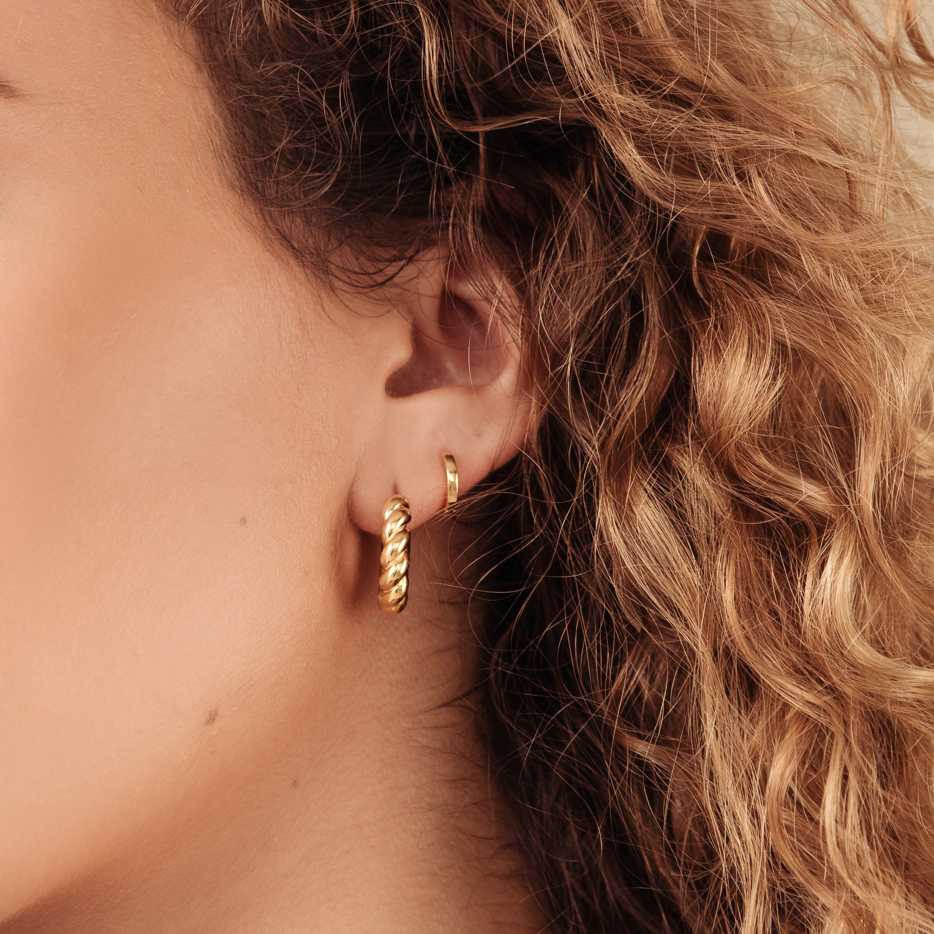 Close-up of a woman's ear with curly hair, wearing classic Editor Huggies in sterling silver—two hoop earrings of different sizes for a minimal aesthetic.