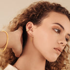 A woman with curly hair wears classic jewelry and stylish Editor Huggies in Sterling Silver.