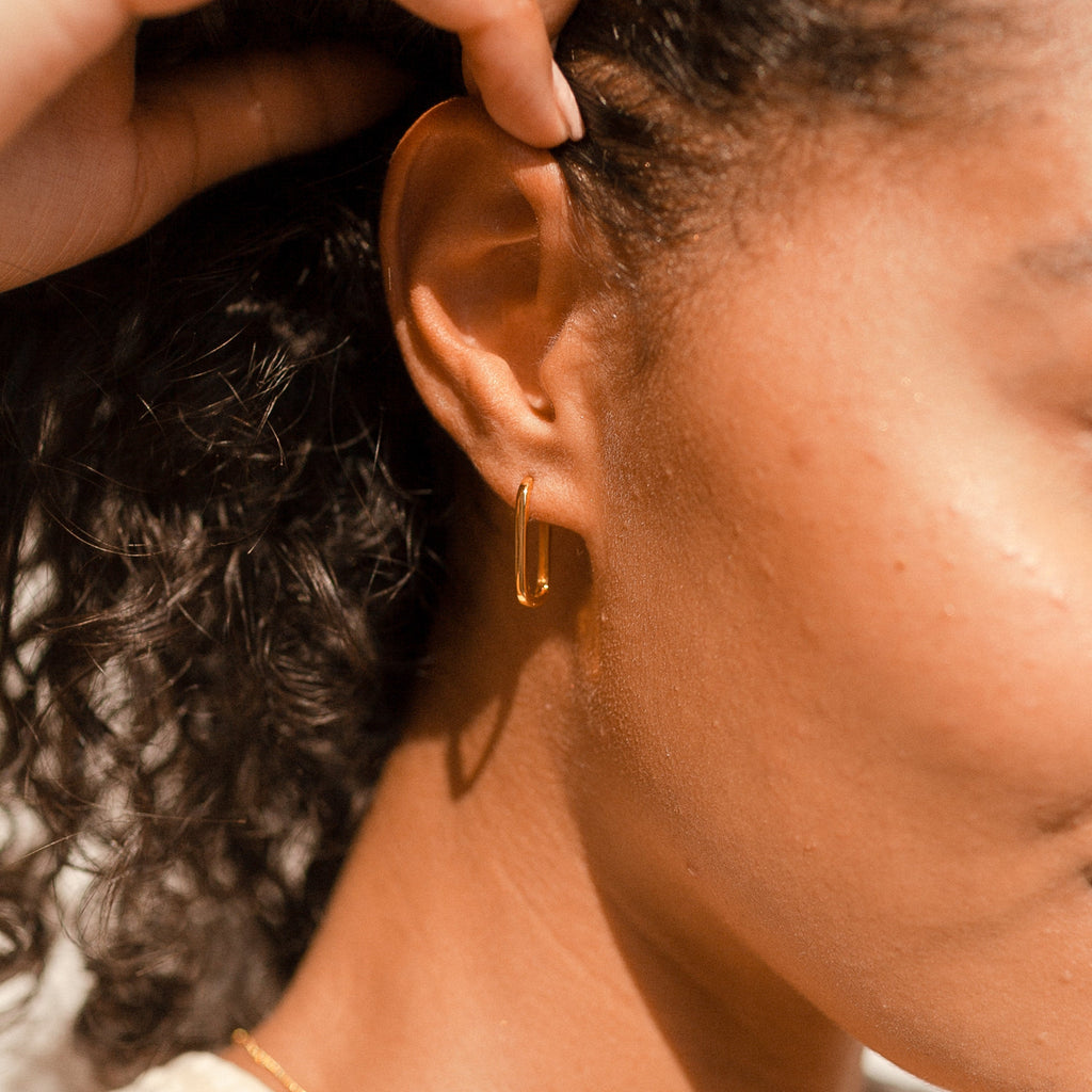 Close-up of a woman's ear wearing a gold hoop from the Linked Earrings Set, her curly hair pulled back by her hand.