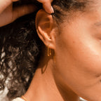Close-up of a woman's ear wearing a gold hoop from the Linked Earrings Set, her curly hair pulled back by her hand.
