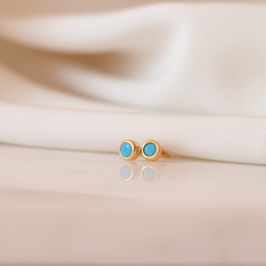 Gold earrings with turquoise stones on a beige fabric background
