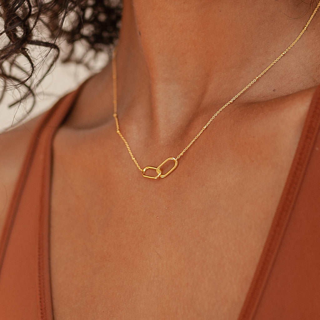Close-up of a woman wearing the Linked Necklace & Earrings Set, featuring two interlocking gold oval links, paired with a brown top.