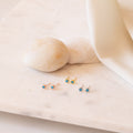 Set of gold, silver and rose gold stud earrings with blue gemstones on a soft beige fabric background