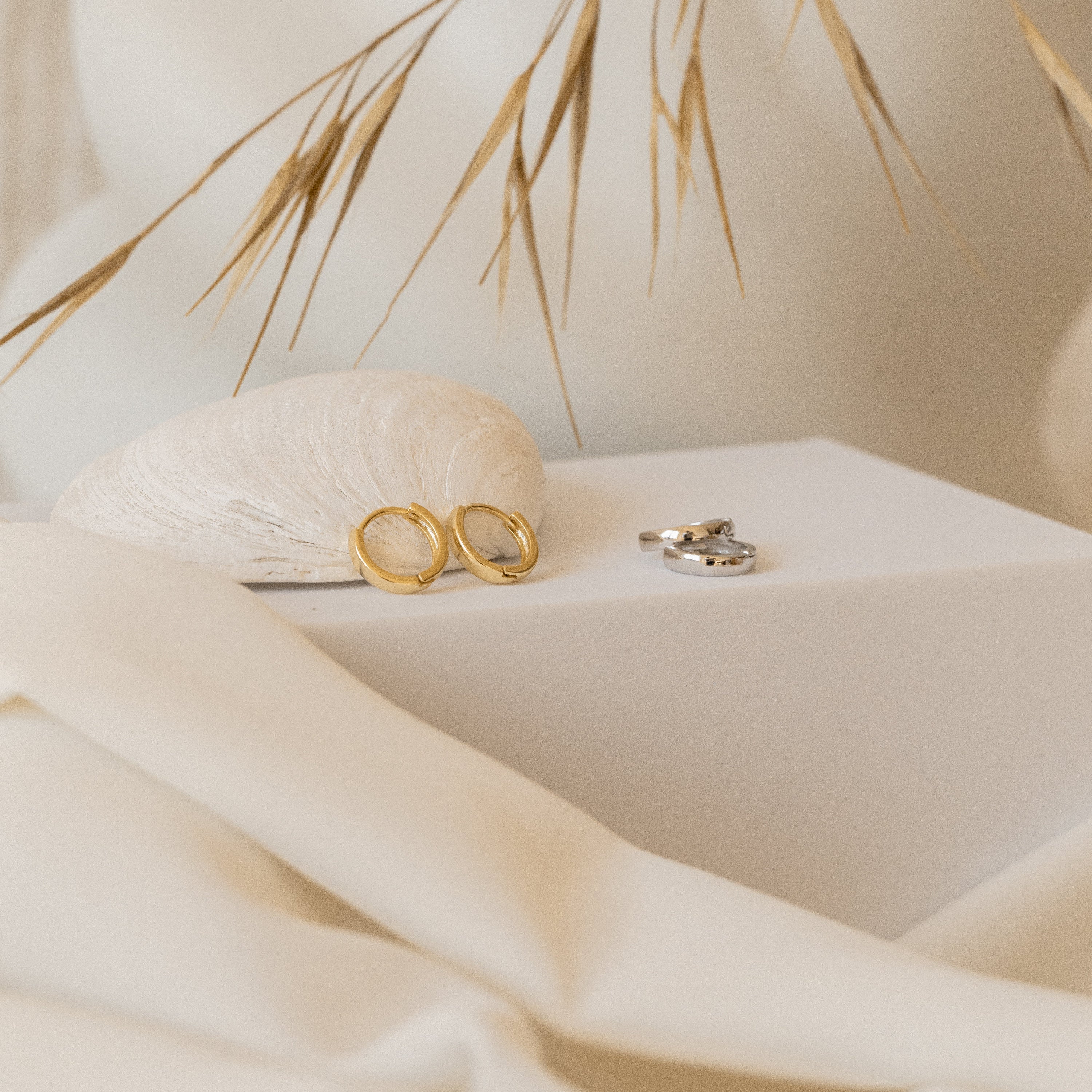 Editor II Huggies and classic hoops in gold and silver are displayed on a white surface with neutral decor, creating a timeless jewelry look.