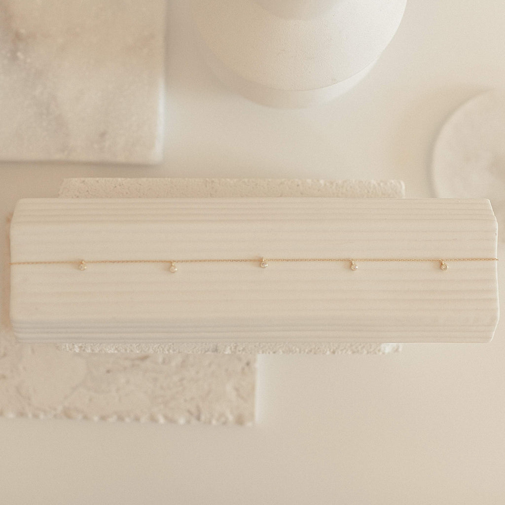 Diamond Station Necklace displayed on a textured white surface in soft lighting, highlighting its modern elegance and timeless appeal.