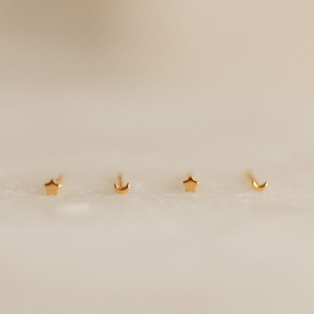 Four gold earrings shaped like stars and moons on a beige background