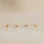 Four gold earrings shaped like stars and moons on a beige background