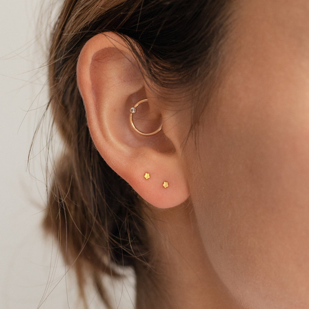 Close-up of a woman's ear wearing the Tiny Moon & Star Studs in her lobe and a small hoop in her cartilage—perfect constellation-inspired jewelry for celestial style lovers.