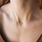A close-up of the Opal Eye Necklace, featuring a small gold oval pendant on a womans neck, worn as a lucky talisman.
