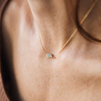 The Opal Eye Necklace, featuring a delicate gold chain and small opal eye pendant, rests gracefully on a womans neck.