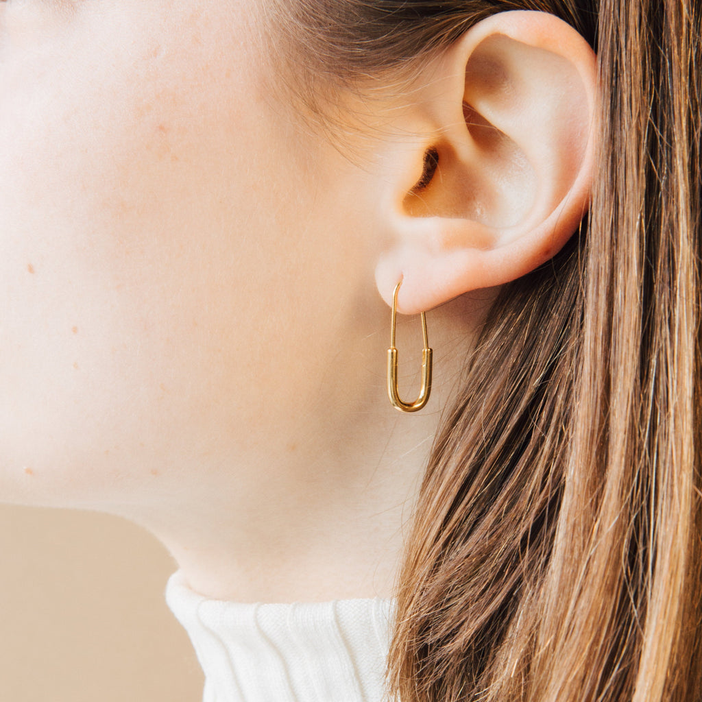 Close-up of an ear with light skin and brown hair wearing a gold Safety Pin Earrings Set in a minimalist U-shape.