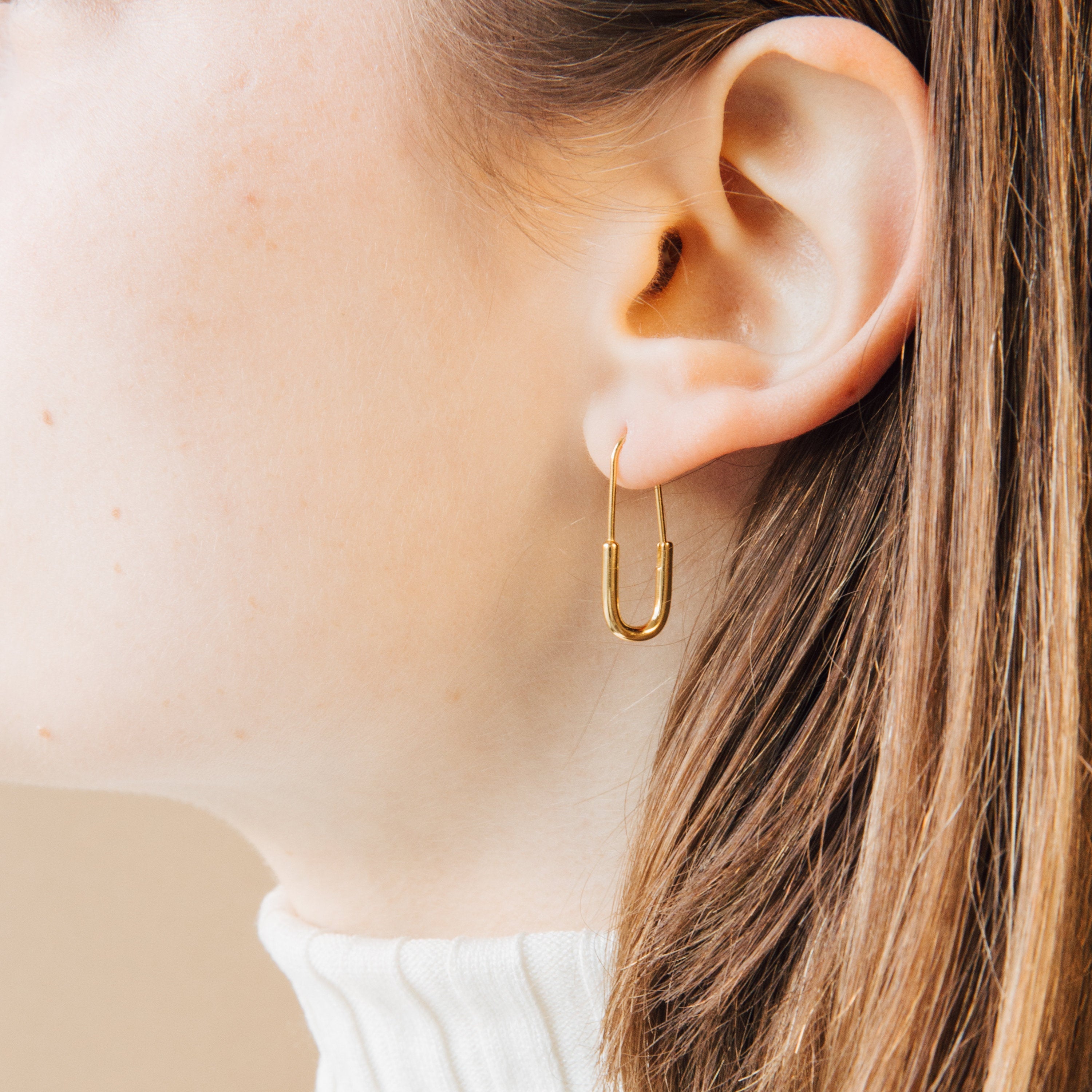 Close-up of an ear with light skin and brown hair wearing a gold Safety Pin Earrings Set in a minimalist U-shape.
