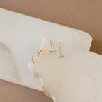 Two pairs of gold and silver stud earrings on a white stone surface with a beige background