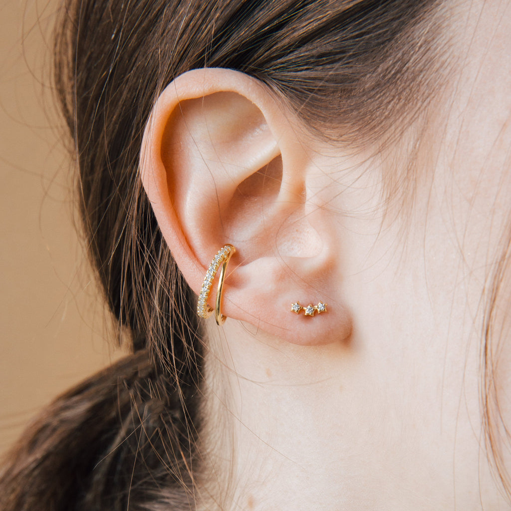 Close-up of a model wearing diamond gold cuff earrings and star stud earrings against a neutral background