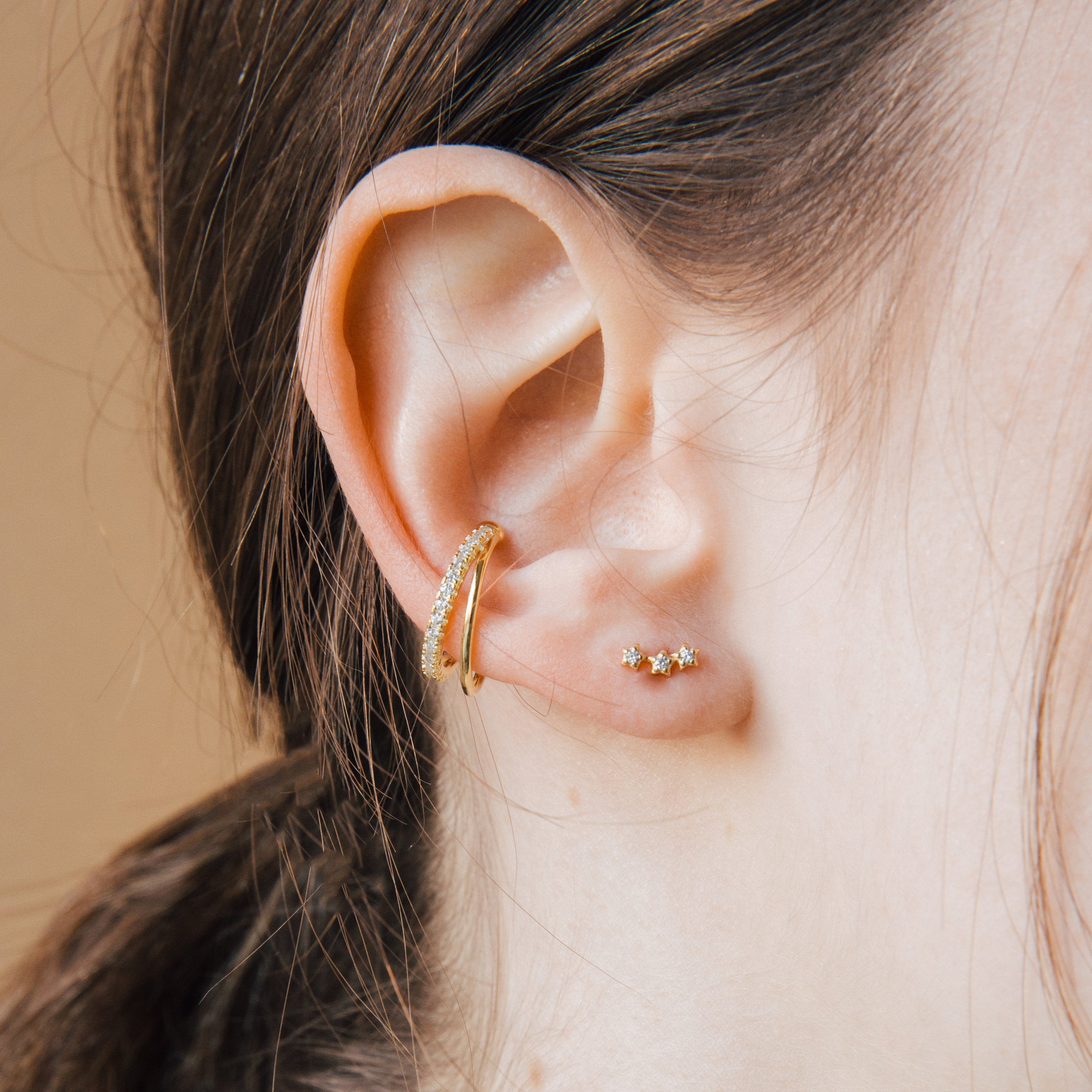 Close-up of a model wearing diamond gold cuff earrings and star stud earrings against a neutral background