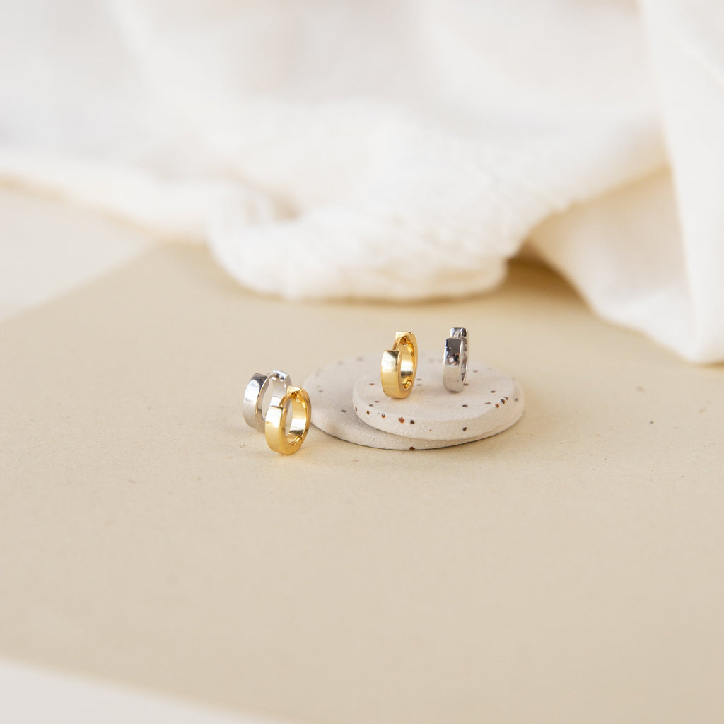 Meg Huggies in Sterling Silver earrings displayed on a round stone with a neutral fabric background.