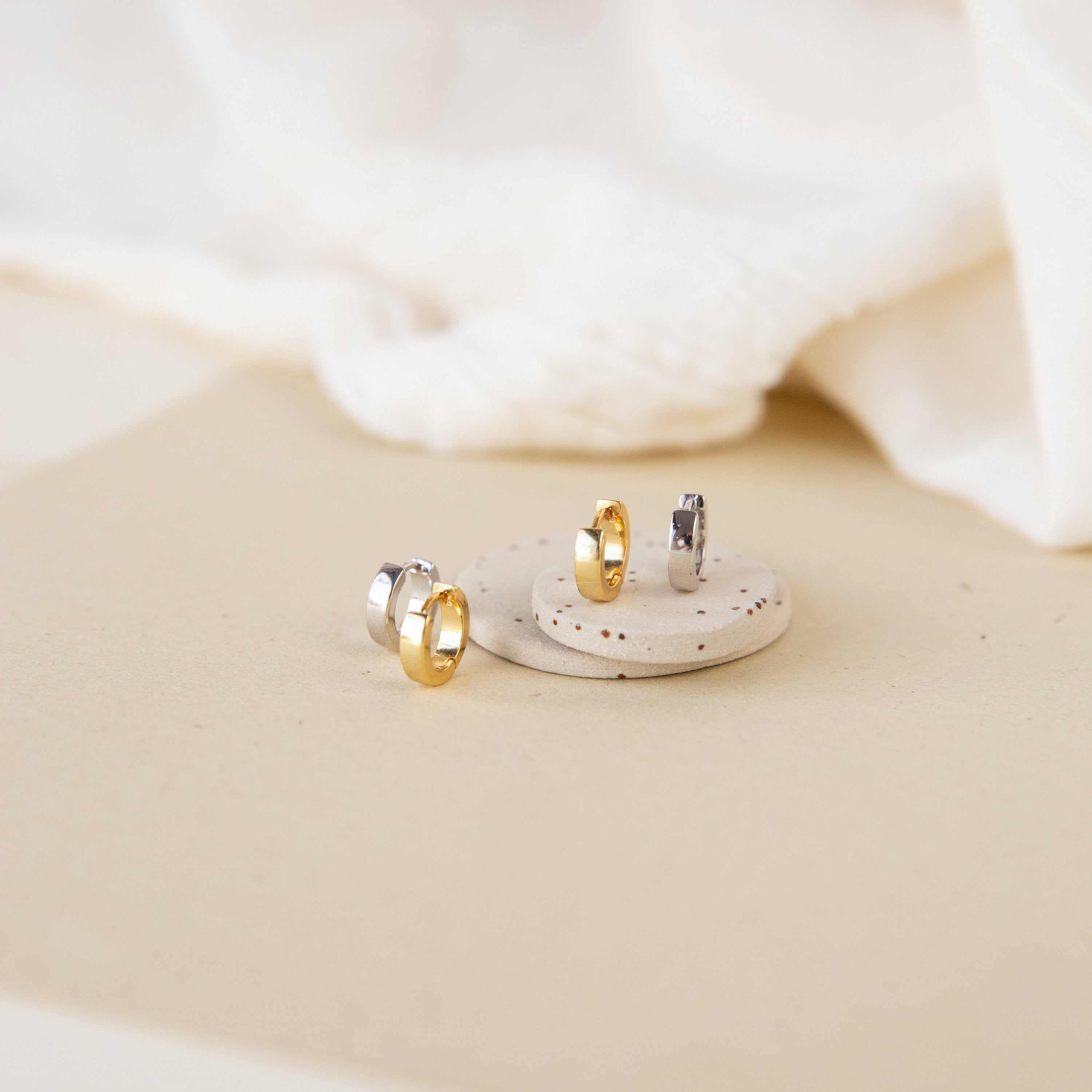 Meg Huggies in Sterling Silver earrings displayed on a round stone with a neutral fabric background.
