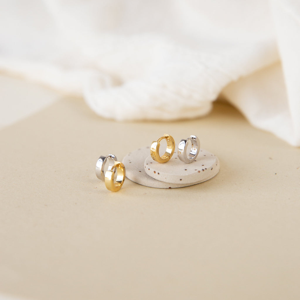 A pair of Meg Huggies in Sterling Silver displayed on a beige stone with soft fabric in the background.