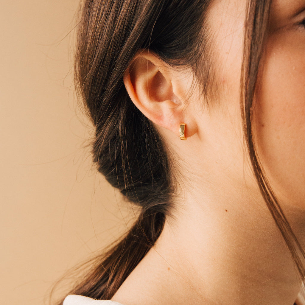 Close-up of a woman’s ear wearing Meg Huggies in 18K Gold, with her hair tied back.