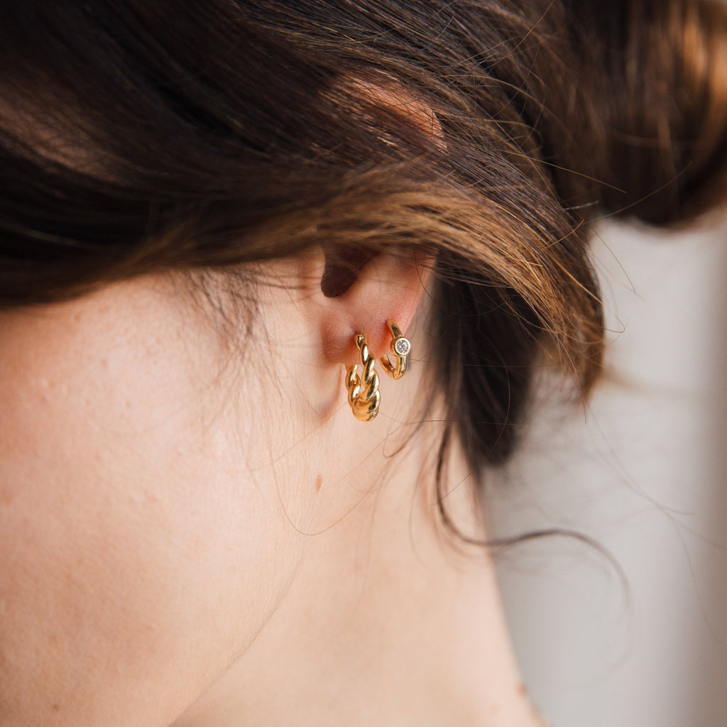 Close-up of a woman's ear wearing Naomi Twisted Hoops and a small stud earring, her hair loosely tied back.