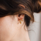 Close-up of a woman's ear wearing Naomi Twisted Hoops and a small stud earring, her hair loosely tied back.