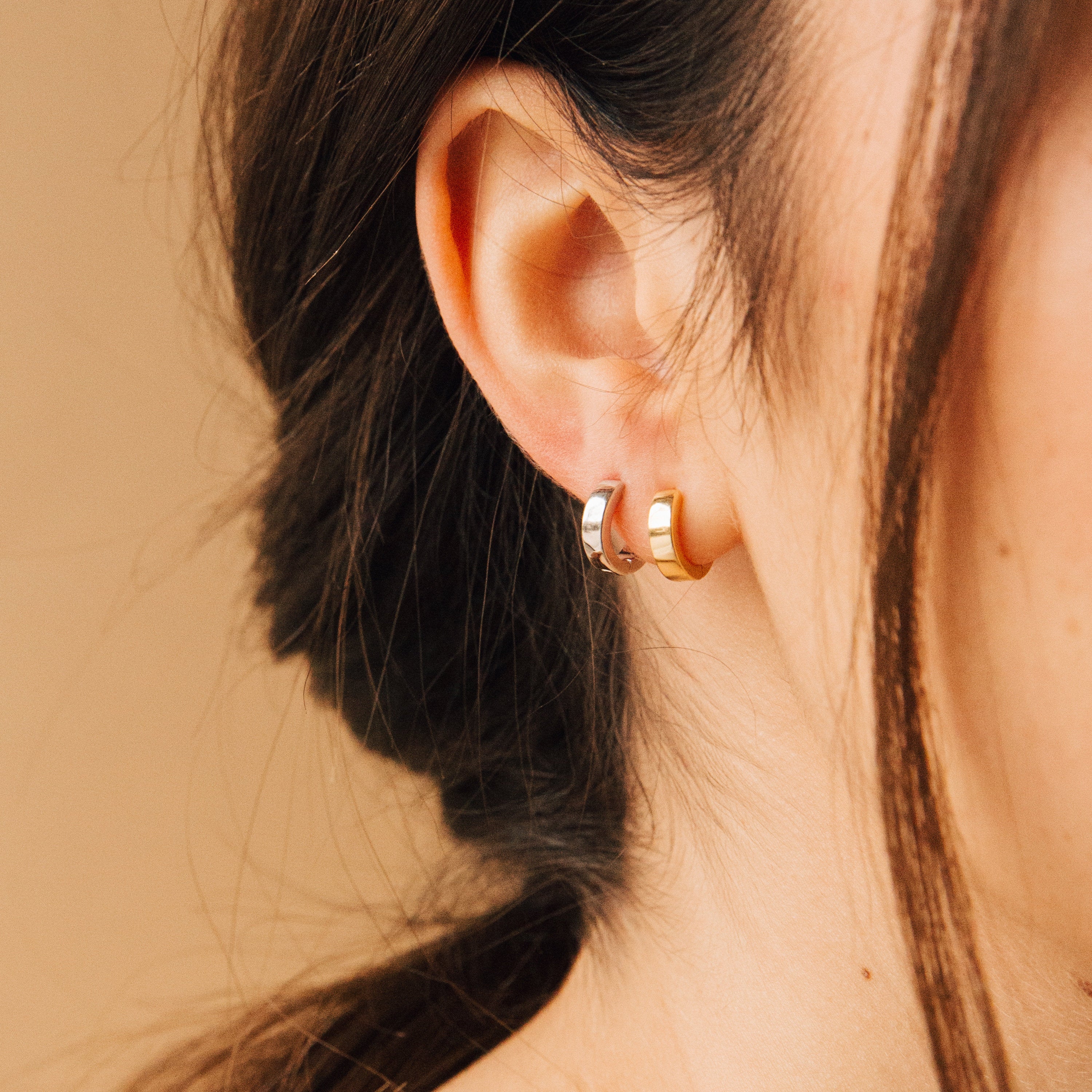 Close-up of a woman's ear wearing two Meg Huggies in 18K Gold, hair tied back against a neutral background.